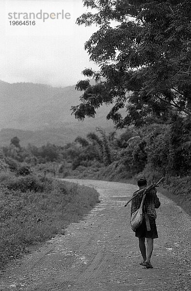 Ein Mann geht auf einer unbefestigten Straße nach Hause  nachdem er in den Reisfeldern von Vang Vieng  Laos  gearbeitet hat.