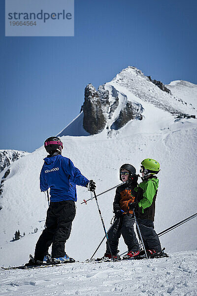 Zwei junge Skifahrer mit ihrem Skilehrer blicken auf eine weite Aussicht.