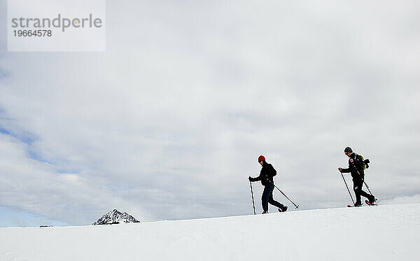 Zwei Personen wandern an einem bewölkten Tag mit Schneeschuhen entlang eines Bergrückens.