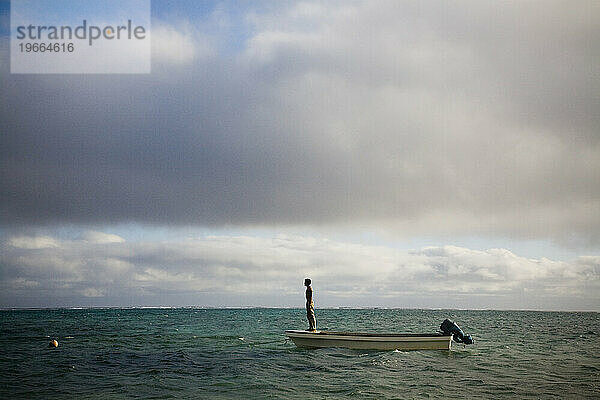 Ein junger Mann steht auf der Vorderseite eines kleinen Bootes vor der Küste abgelegener Inseln im Südpazifik.