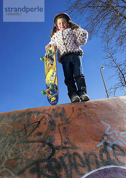 Junges Mädchen steht mit Skateboard und blickt in den Skateboardpark  Santa Fe  New Mexico.