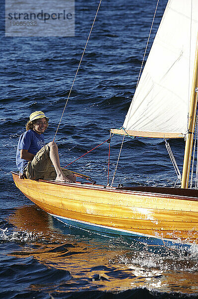 Ein fröhlicher Teenager fliegt durch das Wasser und segelt in einem klassischen Holzboot in der späten Nachmittagssonne in der Penobscot Bay in M