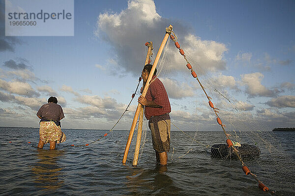 Ein Mann hält die Enden eines Netzes  während eine Frau alle gefangenen Fische einsammelt.