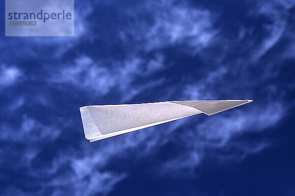 Papierflieger fliegt gegen blauen Himmel.