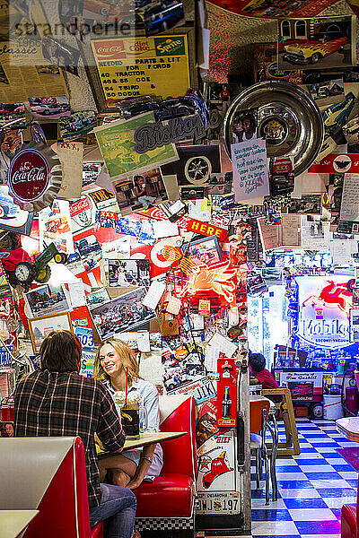 Ein Paar isst in einem Fast-Food-Restaurant im Stil der 1950er Jahre  dessen Wände voller Vintage-Sammlerstücke sind.