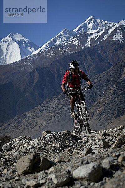 Ein Mann fährt mit dem Mountainbike über Felsen mit schneebedeckten Bergen im Hintergrund.
