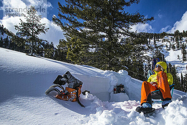 Eine junge Frau entspannt sich nach einer Skitour und dem Ausheben von Lawinengruben