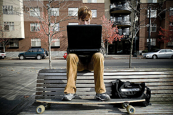 Ein Mann sitzt auf einer Parkbank und arbeitet an seinem Laptop.