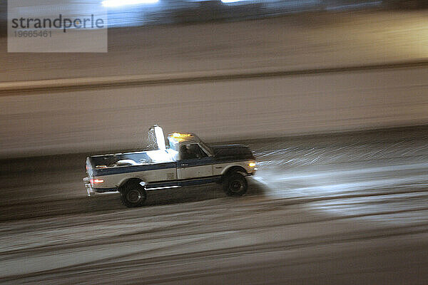 Ein Pickup rast nachts im Schnee über eine Autobahn.