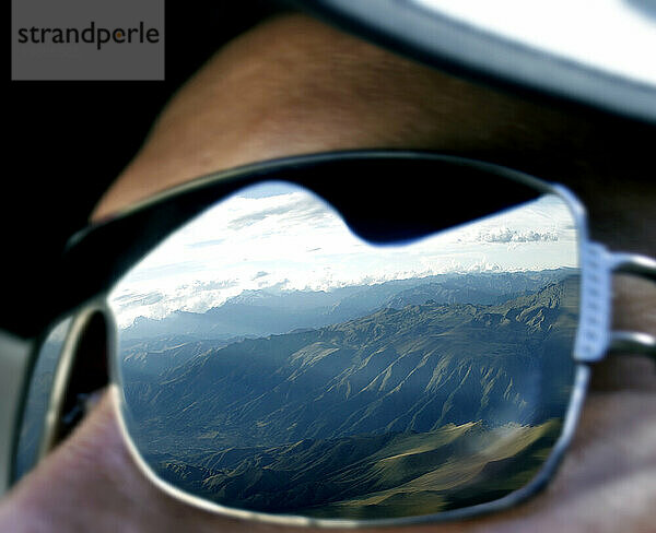 Ein Mann blickt auf die Anden  während seine Sonnenbrille das Spiegelbild der Bergketten Perus einfängt.