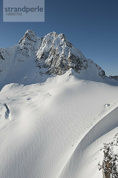 Heliskifahrer steigen unter blauem Himmel einen Gletscher hinab.