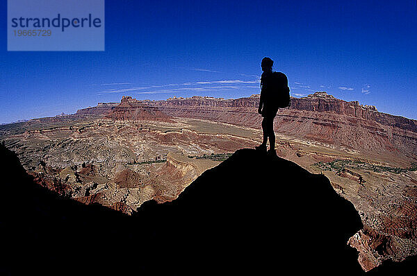 Silhouette einer Frau  die auf einem Felsen steht und über die Wüste blickt