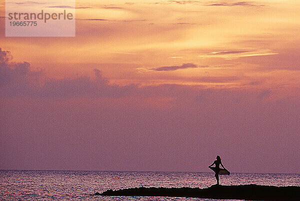 Eine Silhouette einer Frau am Strand bei Sonnenuntergang.