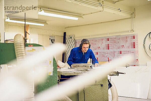 Fokussierter junger Handwerker  der in der Fabrik mit Ohrenschützern arbeitet