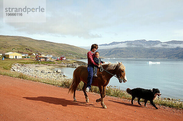 Frau reitet mit ihrem Baby auf einem Pferd in Qassiarsuk  Südgrönland.