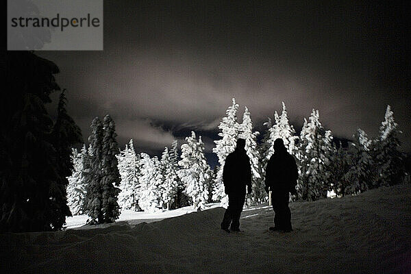 Zwei Männer stehen nachts als Silhouette im Schnee auf dem Mt. Hood in Oregon.