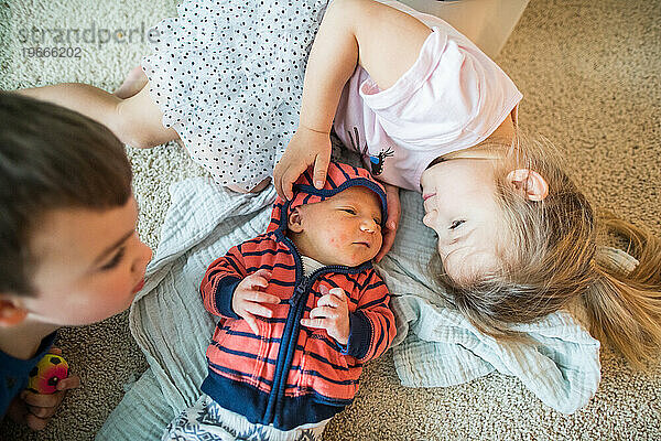 Älterer Bruder und ältere Schwester kuscheln mit ihrem neuen kleinen Bruder.