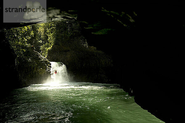 Ein Kajakfahrer springt von einem Wasserfall ab und ist von einer Höhle umgeben.