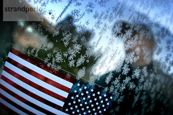 Ein Mann steht hinter einem Aufkleber mit amerikanischer Flagge an einem mit Reif bedeckten Fenster. Arizona  2005. (Selektiver Fokus)
