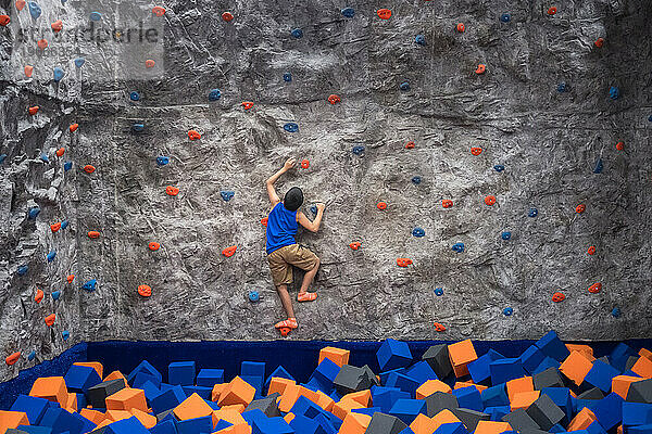 Entschlossener Junge erobert eine Kletterwand in einem Indoor-Fitnessstudio.