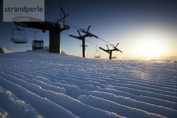 Silhouette eines Sessellifts bei Sonnenaufgang.