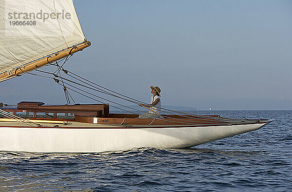 Eine Frau sitzt an der Pinne einer klassischen Yacht und segelt in der schönen Spätnachmittagssonne.