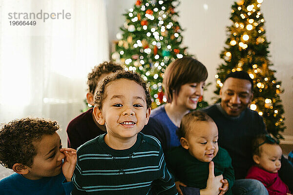 Glücklich lächelnde Kinder mit multiethnischen Eltern am Weihnachtsbaum