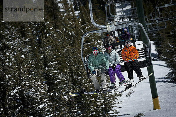 Drei Snowboarder vergnügen sich auf einem Sessellift.