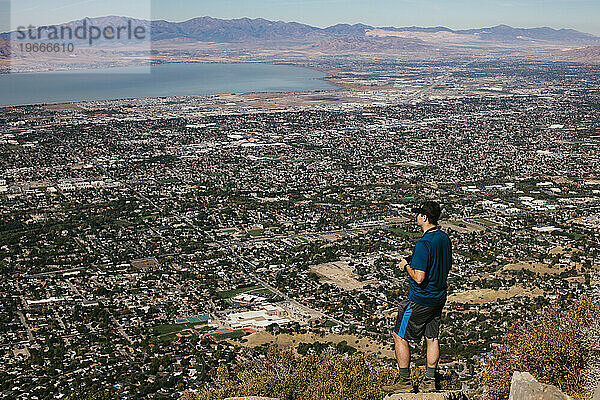 Mann oben auf dem Berg nach der Wanderung mit Blick auf Stadt und See