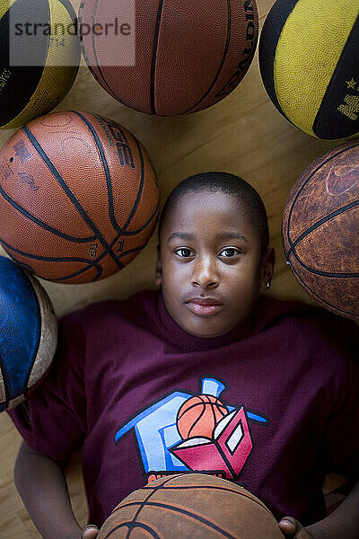 A young boy lies amongst a group of basketballs.