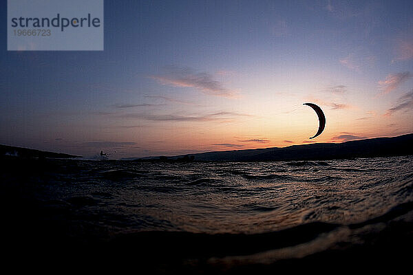 Tiefwinkelperspektive eines Mannes  der in einen Sonnenuntergang kitesurft.