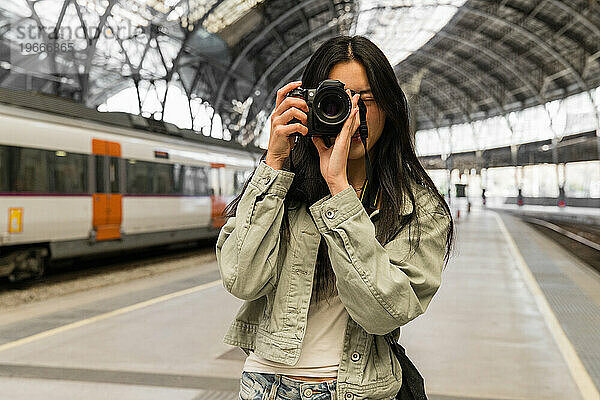 Fotografin macht ein Foto mit einer Kamera in einem Bahnhof.