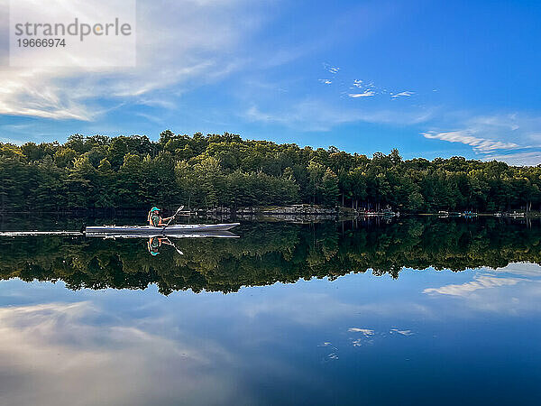 Frau paddelt an einem Sommertag allein Kajak auf einem ruhigen See.
