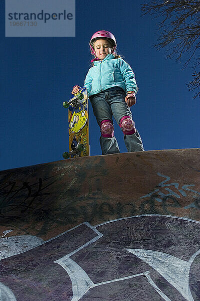 Junges Mädchen steht mit Skateboard und blickt in den Skateboardpark  Santa Fe  New Mexico.