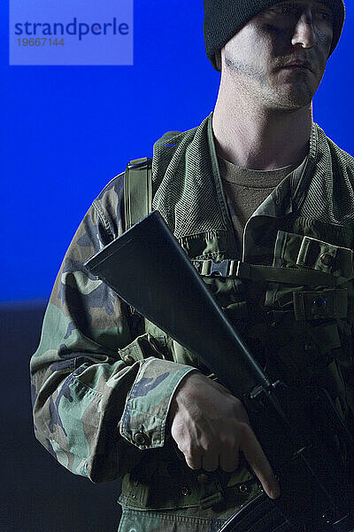 Ausgeschnittene Vorderansicht eines stehenden Soldaten in Tarnkleidung und Hut  der ein Gewehr vor sich hält. (Veröffentlichungscode: rrk_mr27)