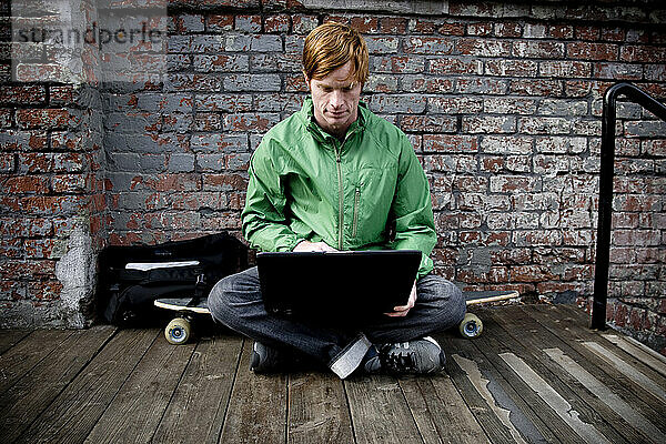 Ein Mann sitzt vor einer Ziegelwand und arbeitet an seinem Laptop.