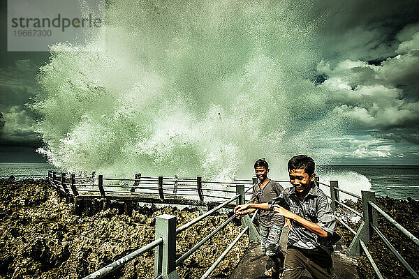 Zwei indonesische Jungen laufen vor einer Welle davon