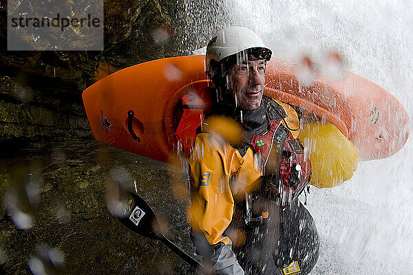 Attraktiver männlicher Kajakfahrer  der unter einem Wasserfall steht.