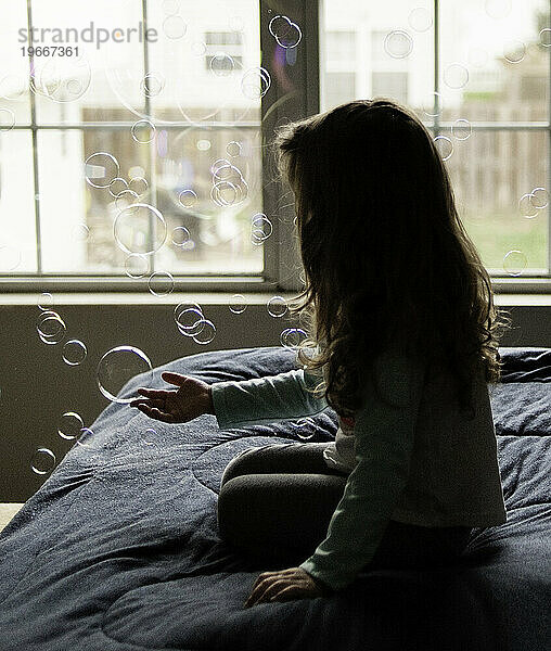 Kleines Mädchen fängt Seifenblasen im Schlafzimmer