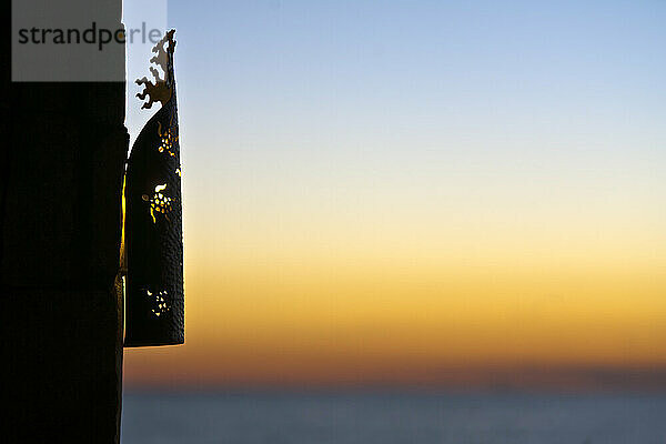 Ein Laternengitter an einer Wand  Silhouette vor dem Sonnenuntergangshimmel.