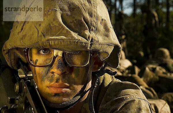 Ein Marinerekrut hält während einer Feldübung seine vom Militär ausgegebene Brille mit Klebeband zusammen. Er trägt eine Wüstentarnuniform und einen Helm.