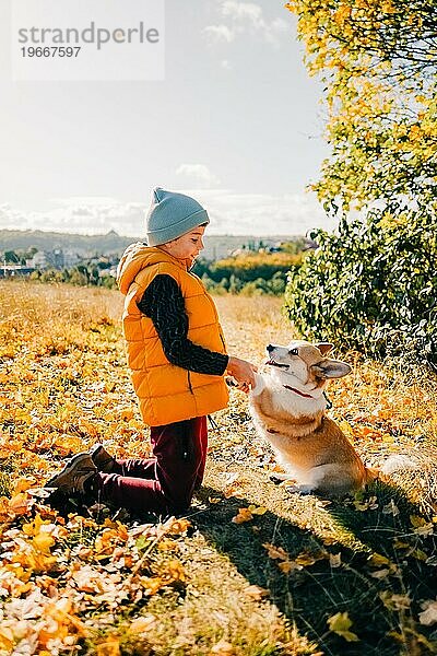 Ein Junge geht mit einem Corgi-Hund im Herbstwald spazieren