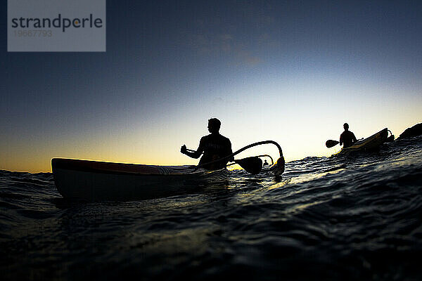 Silhouette von drei Auslegerkanu-Paddlern bei Sonnenuntergang aus der Perspektive eines niedrigen Winkels.