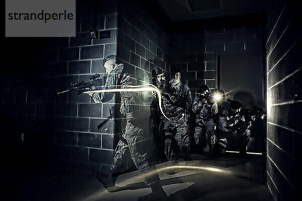 In völliger Dunkelheit bewegen sich Angehörige der Sicherheitskräfte der Luftwaffe während des Geiseltrainings taktisch durch ein Gebäude und nutzen dabei nur die an ihren Waffen angebrachten Taschenlampen.