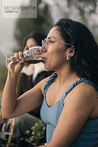 Schöne hispanische junge Frau  die draußen Rotwein trinkt