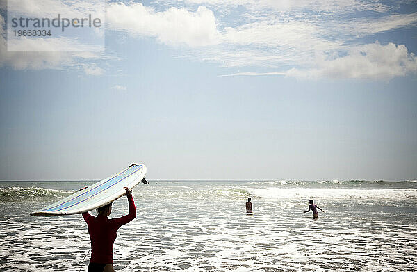 Eine Frau watet mit ihrem Surfbrett auf dem Kopf hinaus ins Meer.