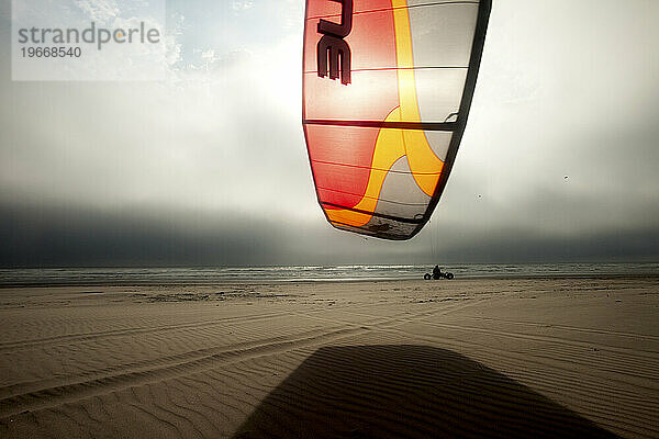 Silhouette eines männlichen Drachenbuggys (Drachenbuggy)  der in bedrohlichen Wolken und ungewöhnlichem Licht den Strand hinunterrollt.