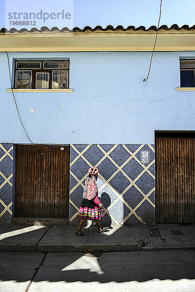 Eine junge Quechuan-Frau betritt einen einsamen sonnigen Platz in einer schattigen Straße in Urubamba.