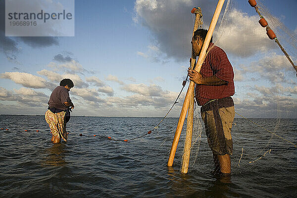 Ein Mann hält die Enden eines Netzes  während eine Frau alle gefangenen Fische einsammelt.