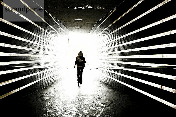 Eine Frau geht durch einen Gedenktunnel mit beleuchteten Lichtstreifen.